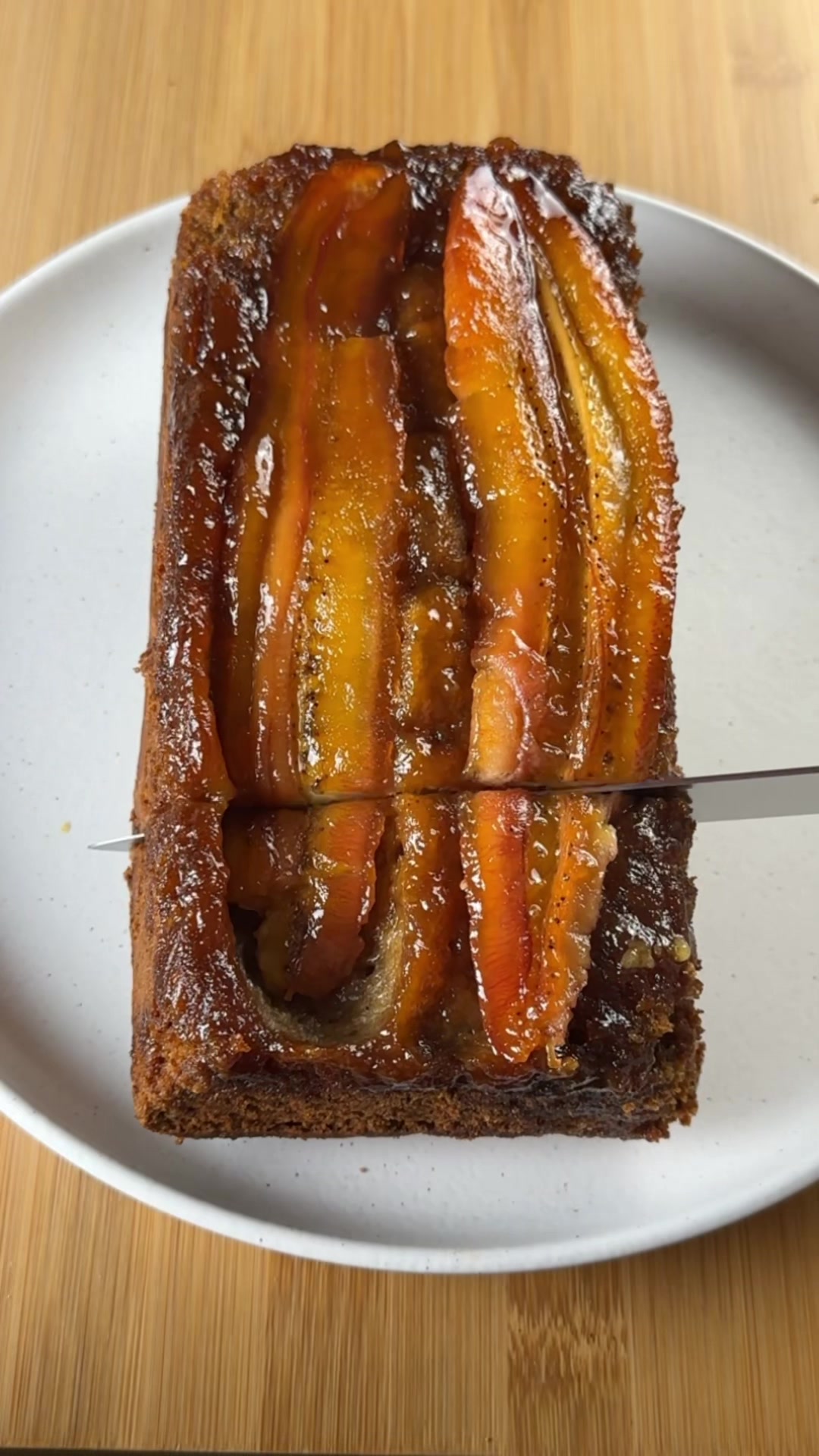 RECIPE: banana upside down cake🍌 In this highly requested recipe, an upside down cake meets chocolate chip banana bread to make the perfect dessert. let me know if you give this recipe a try🤍 . CAKE: 3 ripe bananas, mashed  1 c brown sugar 1/2 cup milk of choice  2 eggs 1/4 cup greek yogurt or sour cream 1 tsp vanilla extract  1/2 cup oil 2 cups all purpose flour 1/2 tsp salt 1 tsp baking soda 1 1/2 tsp cinnamon ASSEMBLY: 3/4 cup white sugar 1/3 cup water 3 bananas, (sliced down the middle) . Preheat oven to 350 degrees Fahrenheit. In a large bowl, whisk together mashed bananas, brown sugar, milk, vanilla, oil, yogurt, and eggs. Add flour, baking soda, cinnamon, and salt. Fold until everything is combined.  Grease an 8x8 square pan well with oil or nonstick cooking spray and line with parchment paper, leaving overhang on each side for easy release of the cake. In a small/medium sauce pan add the sugar and water. Turn the stove on medium heat, swirling the pan constantly until the caramel is bubbling and reaches an amber color. Place your sliced bananas face down in a line on the greased, parchment lined pan. Pour the caramel over top. Scoop the batter over top and spread out. Bake the cake in the preheated oven for 40-42 minutes or until a toothpick comes out with a few moist crumbs. When the cake comes out of the oven, run around the sides of the pan with an offset spatula to release the edges. Let the cake cool for 5 minutes before running around the sides with an offset spatula again and inverting it onto a serving plate. Enjoy! #banana #upsidedowncake #bananabread